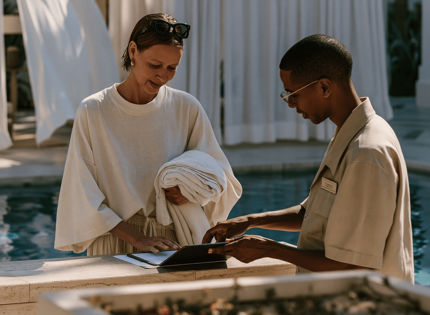 A staff member helping a guest sign up on a tablet by the pool